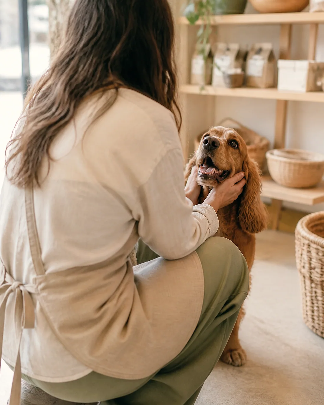 Mağazada bir köpeği selamlayan, keten önlüklü dükkân sahibi